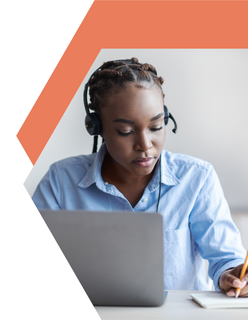 A woman wearing a headset sits at a desk, looking at a laptop and writing on paper. She is focused, and the background includes an abstract orange geometric shape.