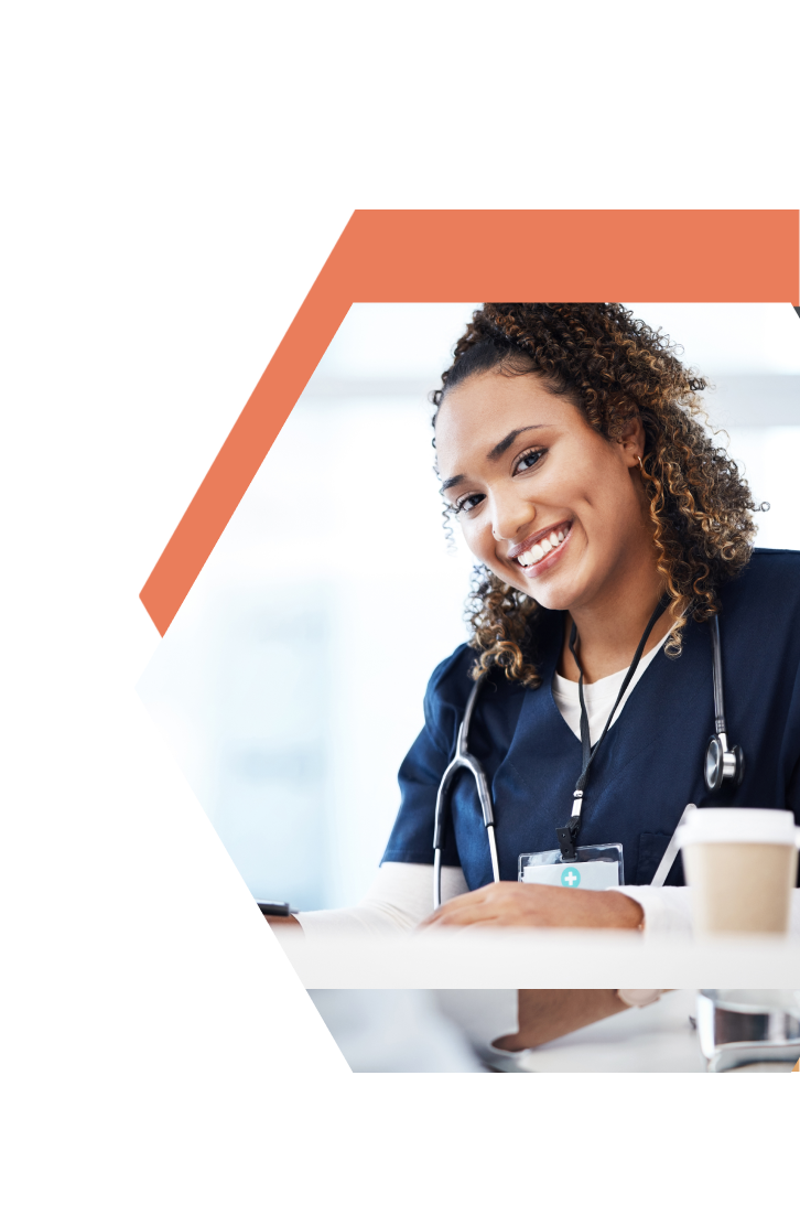 A smiling healthcare professional in navy blue scrubs, representing CNA Training in Lakes Country Minnesota, sits at a desk with a coffee cup and stethoscope, framed by an orange hexagon.